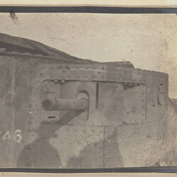 Side view of tank with gun visible, legs of a person standing on the tank above.