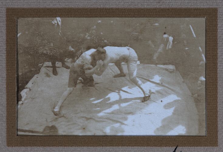 Two men wrestling in ring surrounded by audience.