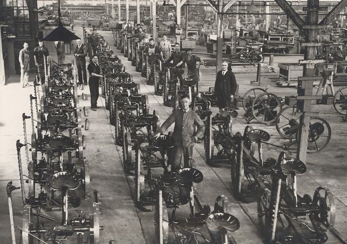 Men stand beside mowers on factory production line.