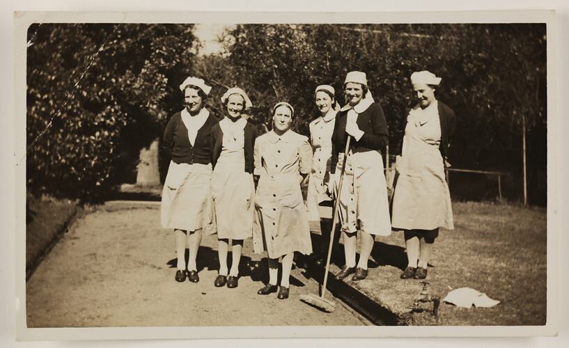 Group of six women standing outside, trees behind.