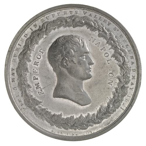 Round silver medal with male facing right.Wreath border. Text around edge.