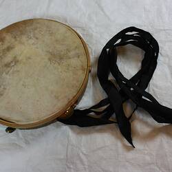 Tambourine, olive frame, natural animal skin. Metal jingles, bells and black ribbon streamers.