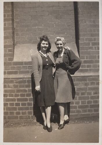 Two girls posing against brick wall.