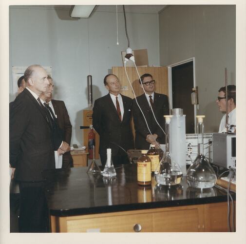 Group of men listening to scientist in lab.
