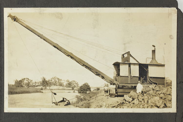 Monochrome photograph of an excavator near a river.