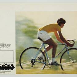 Cyclist riding bicycle wearing yellow top and white shorts. Black printed text at left.