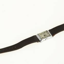Watch with rectangular chrome case. White metal face has black arabic numerals. Black leather band.