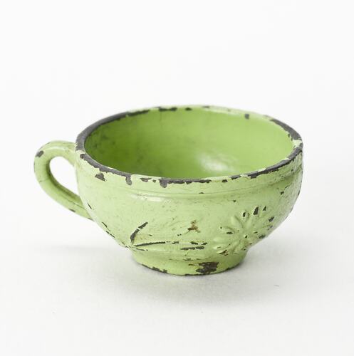 Miniature scuffed green teacup from a doll's house.