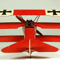 Red aeroplane model. White strip on top of wings with black cross. Rear view.