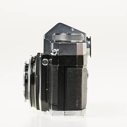 Black camera, metal top section, lens. Dial top corner. Left profile.