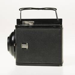 Black cube shaped all metal camera. Carry handle on the top plate. Left profile.