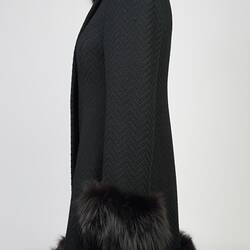Black woollen double-breasted coat with fur collar, cuffs and hem. Left profile.