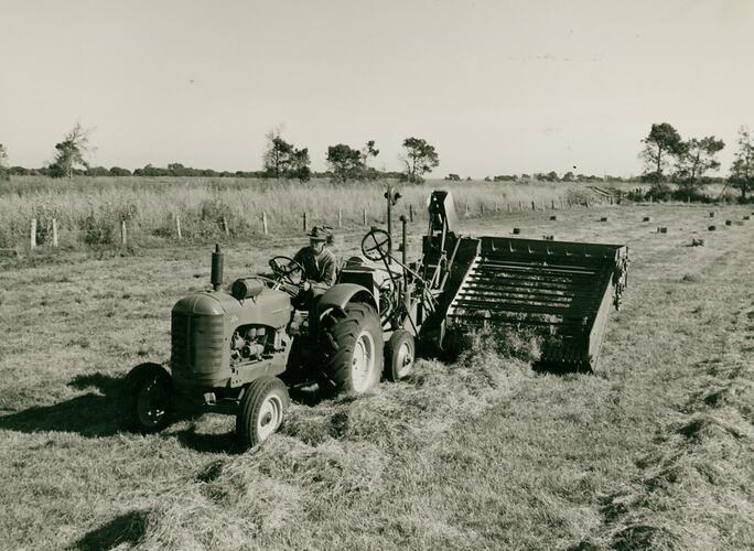 Front view of man driving a tractor towing a pickup baler, in field of windwrown hay.