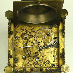 Decorative table clock, square gilded brass case on four feet. Underside view. Engraving detail.
