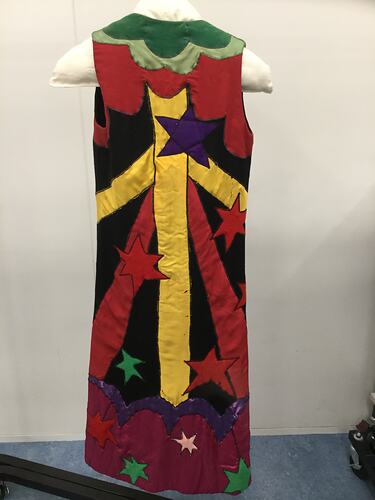 Back of colourful sleeveless coat with stars and shapes. Mostly yellow, red, black and green.
