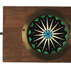 Rectangular wooden box with round coloured glass disc in centre. Turning hand on left side.