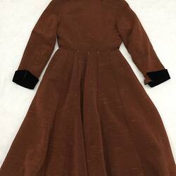 Back of long coat made from a reddish brown ribbed fabric. Laid flat.