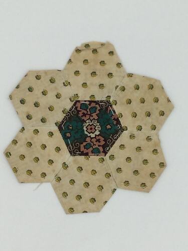 Six (rounded) pointed piece of pale fabric with spots. Dark floral centre.