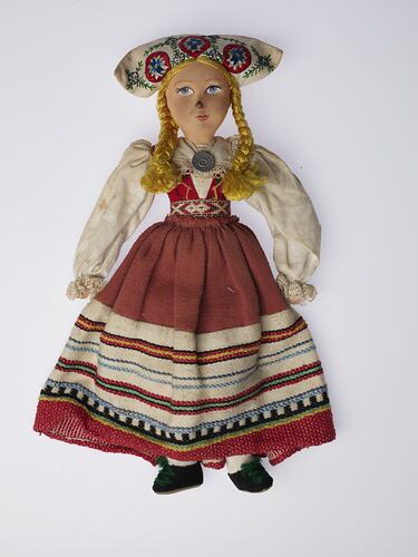 Doll with coloured hat, blonde plaits wearing white shirt and red striped dress.