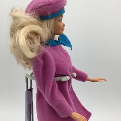 Profile of Barbie doll with blonde hair wearing pink with blue trim coat and hat.
