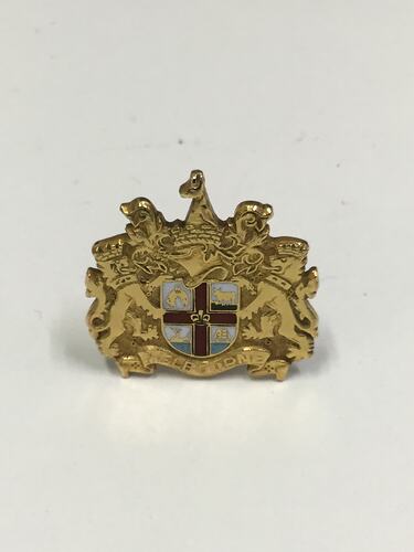 Gold cufflink with central coloured enamel shield. Supported by two lions. Kangaroo amongst scrolled ribbons above.
