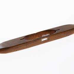 Wooden shuttle with a piece of thick wire through cut out centre. Two wooden rollers underneath shuttle.