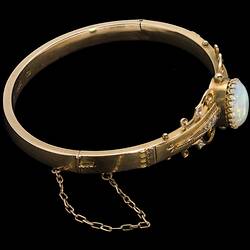 Gold bracelet with central oval white opal, supported by rose cut diamonds and delicate gold filigree-style detail.