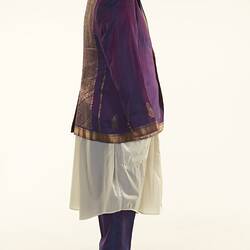 Purple sari two-piece suit and matching tie, long off-white shirt. Gold detail on jacket edging. Right profile