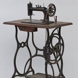 Sewing machine fitted to a metal frame with a wooden bench.