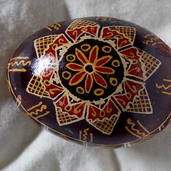 Egg, hand painted on a brown background with yellow, red and white star design at the centre of the egg.