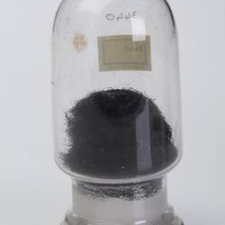 Domed cylindrical jar containing black stringy botanical sample.