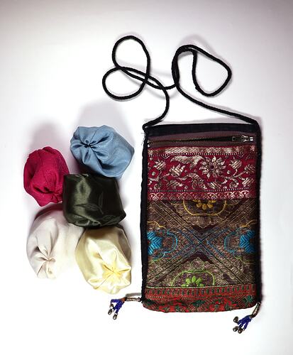 Black patterned fabric sleeve with string. Beside it 5 fabric round jacks in blue, pink, cream, green and white.