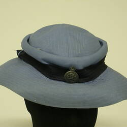Blue hat with black hatband and metal broach, on black mannequin head.