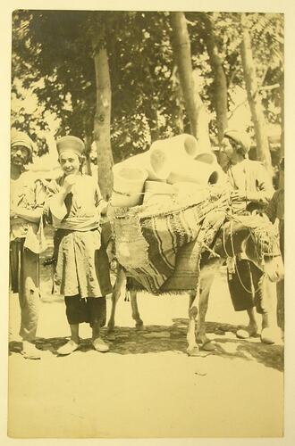Three Arab men with a donkey, which has pots tied to its back.
