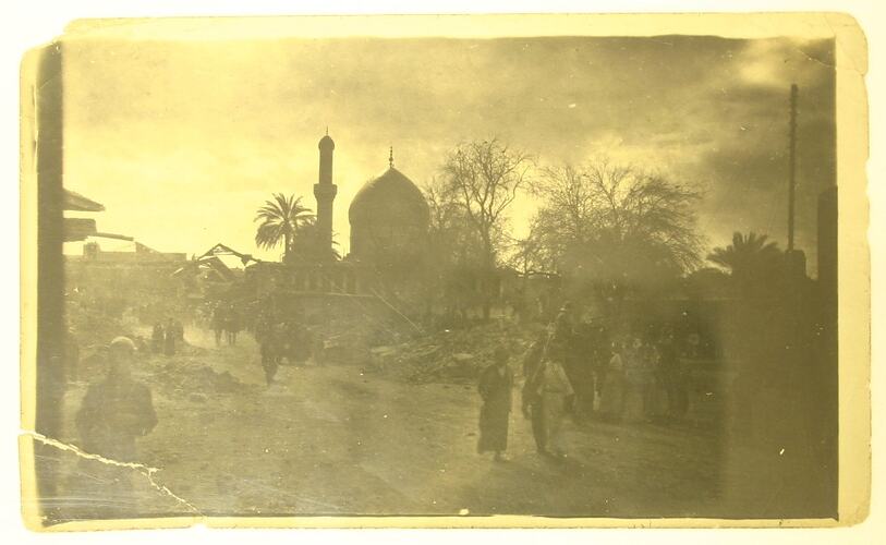 People in a street, mosque dome and minaret in background.