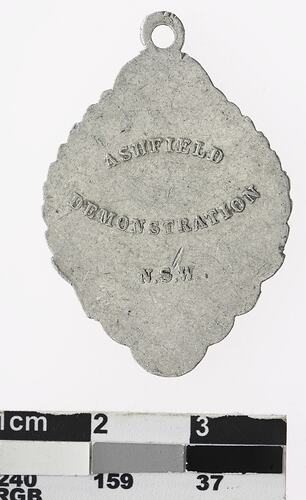 Silver rounded rhombus shaped medal with text in centre.
