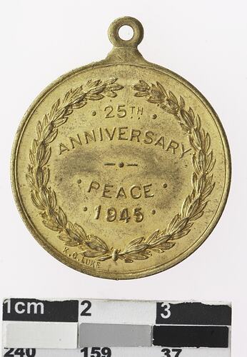 Round gold coloured medal with text and wreath surrounding.