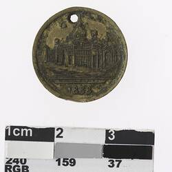 Round gold coloured medal with building and text below.