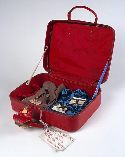 Open red vinyl suitcase with packed contents.