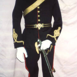 Black military uniform jacket on mannequin, with red collar and gold embroidery waist, front view.