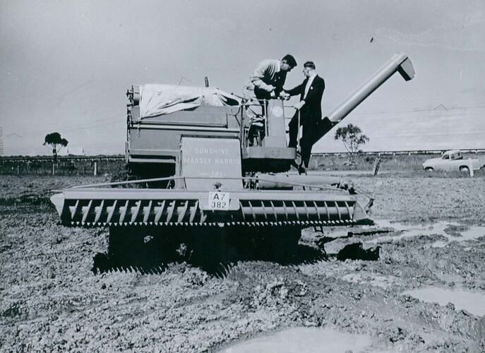 Two men on a harvester in muddy field,