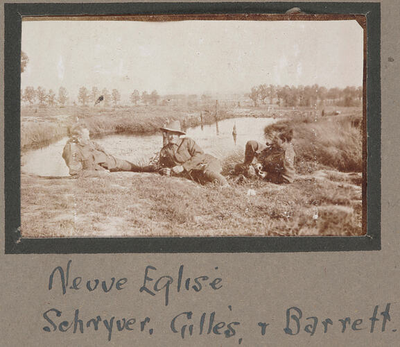 Three servicemen lying on grass in front of a lake, with trees in the background.