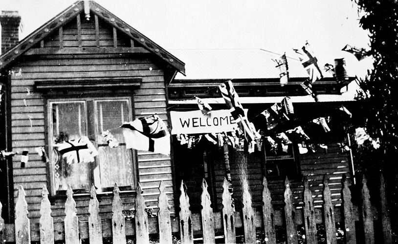 House decorated with flags, bunting and a welcome sign. Picket fence at front.