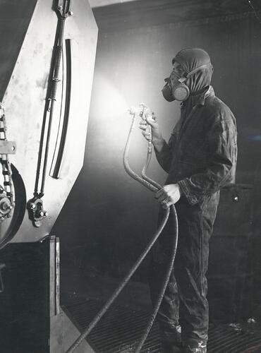 A man in full protective suit and face mask operates a spary gun.