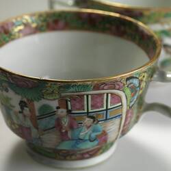 Decorative teacup with colourful Chinese scene that includes three figures. Top angle view.