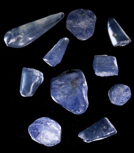 Ten smooth, uncut blue sapphires of uneven shape.