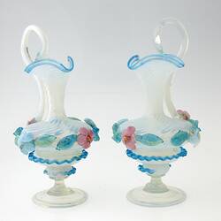 Pair of blue blown-glass ewer, spiral fluted neck, serpentine handle, flattened bulbous body layered with pink, blue, green flowers and leaves.