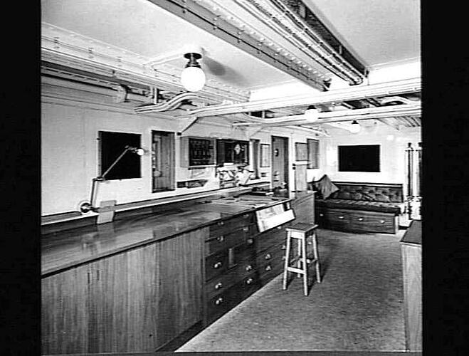 Ship interior. Chart room. Wooden bench lines wall at left.