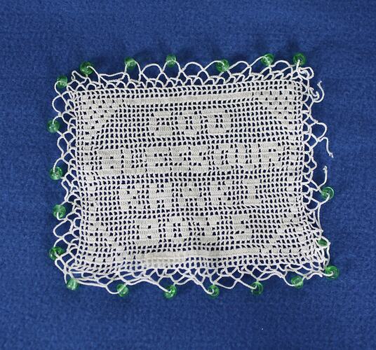 Squair shaped white cotton crocheted doily, motto crocheted in the centre and green beads on all four sides.