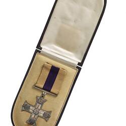 Silver cross shaped medal with purple and white ribbon in open case.
